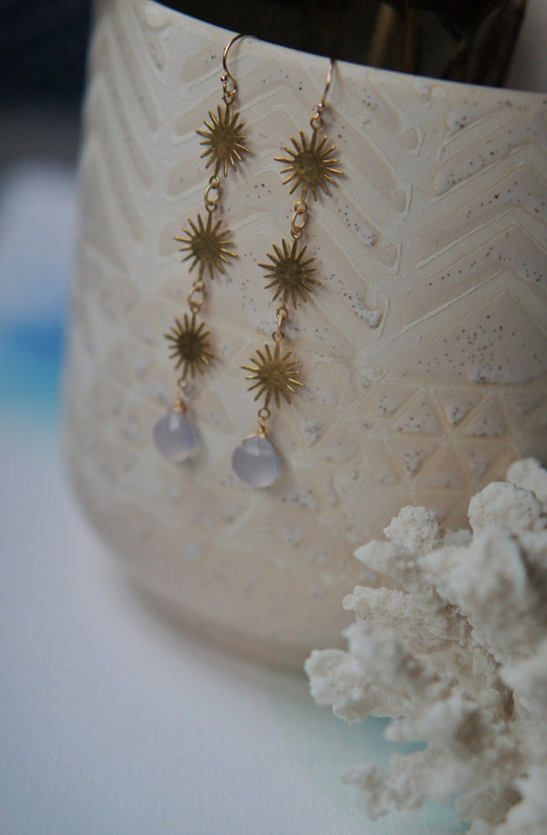 long gold sunburst earrings with chalcedony stones hanging on potted plant