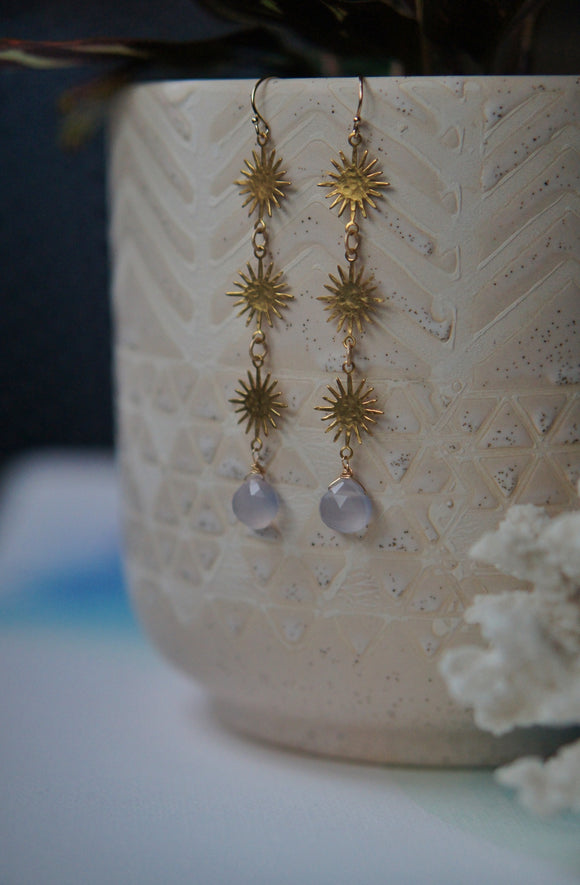 long gold sunburst earrings with chalcedony stones hanging on potted plant