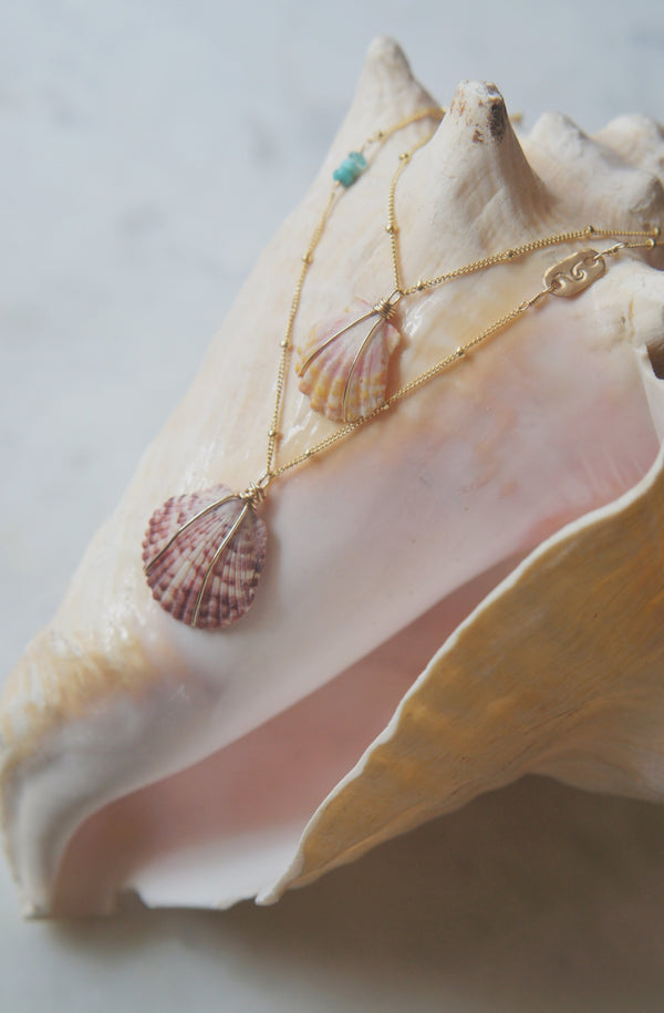 2 necklaces with stamped gold bar, turquoise, and shell displayed on large conche shell