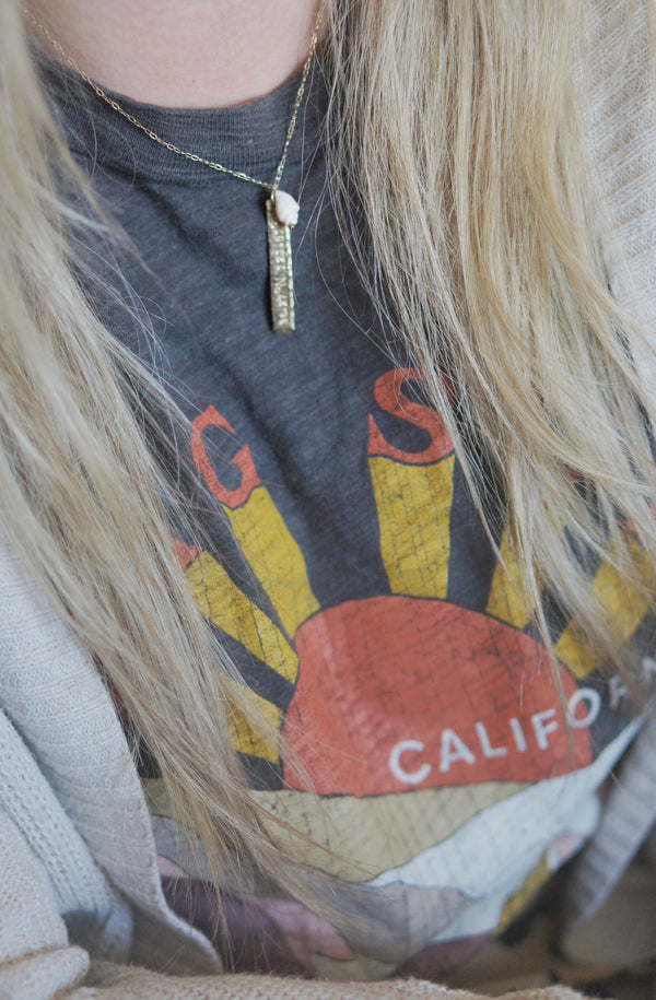 woman wearing happy place necklace with long blond hair in a graphic tee