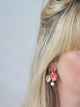 woman with long blond hair wearing coral color carved conche flower earring charm wiht shell earring charm in second ear piercing