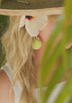 Lime green handpainted shell earrings in a checkered pattern worn by woman with long hair wearing a hat and flower in her hair