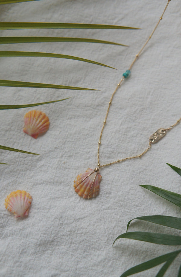 necklace with stamped gold bar, turquoise, and shell  displaed on fabric with leaves