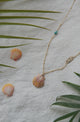 necklace with stamped gold bar, turquoise, and shell  displaed on fabric with leaves