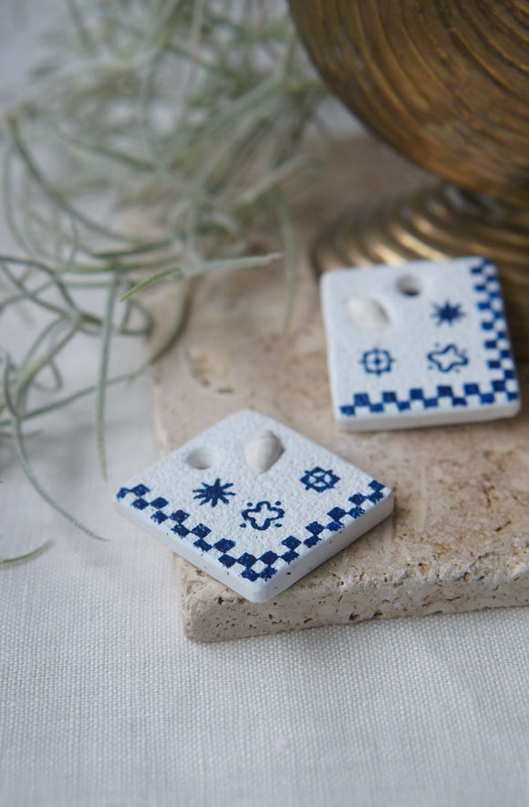 blue and white square clay and shell hoop earring charms displayed on stone