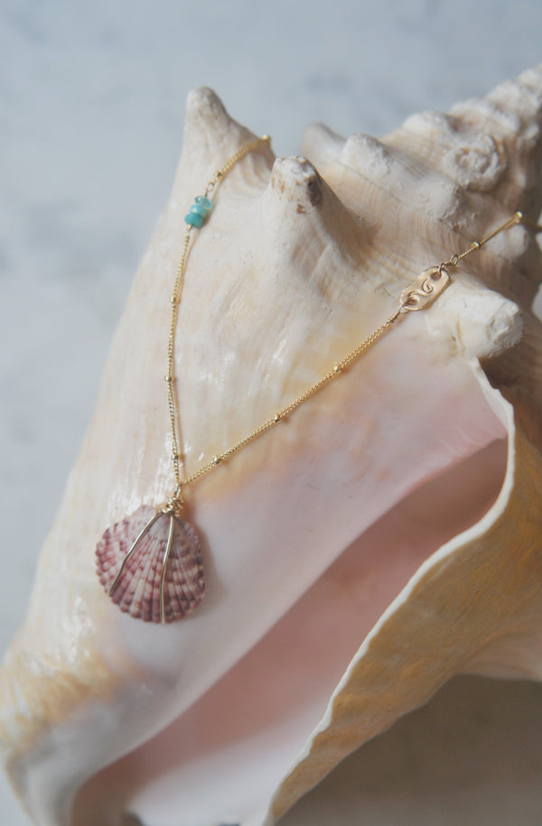 necklace with stamped gold bar, turquoise, and shell displayed on large conche shell