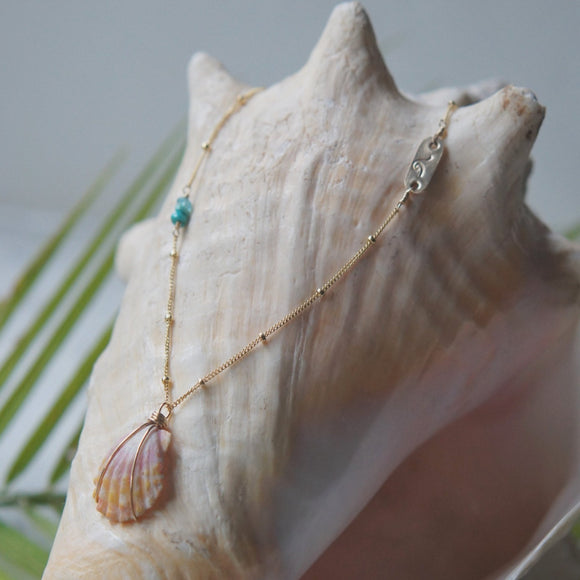 necklace with stamped gold bar, turquoise, and shell displaed on large conche shell