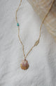 necklace with stamped gold bar, turquoise, and shell displayed on fabric