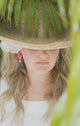 Woman wearing carved conch flower, freshwater pearls and nassa shell earring charms with hat and flower in her hair