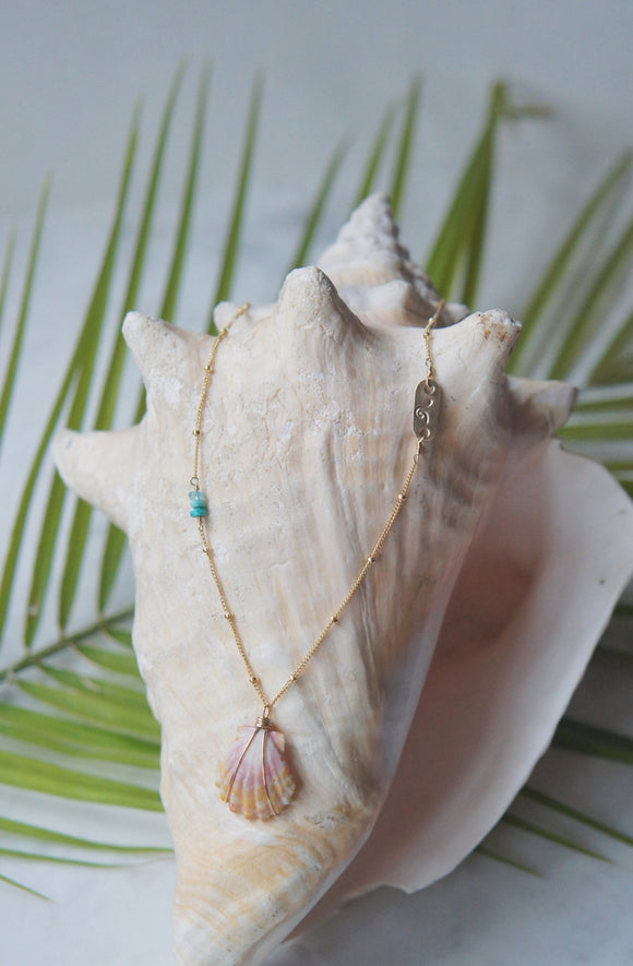 necklace with stamped gold bar, turquoise, and shell displayed on large conche shell