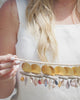 Woman holding branch featuring gold, shell, and drift wood earring pairs