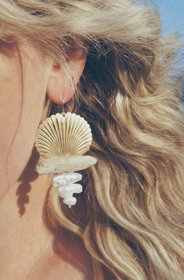 Gold shell, driftwood, and freshwater pearl earrings worn by woman with long blond hair