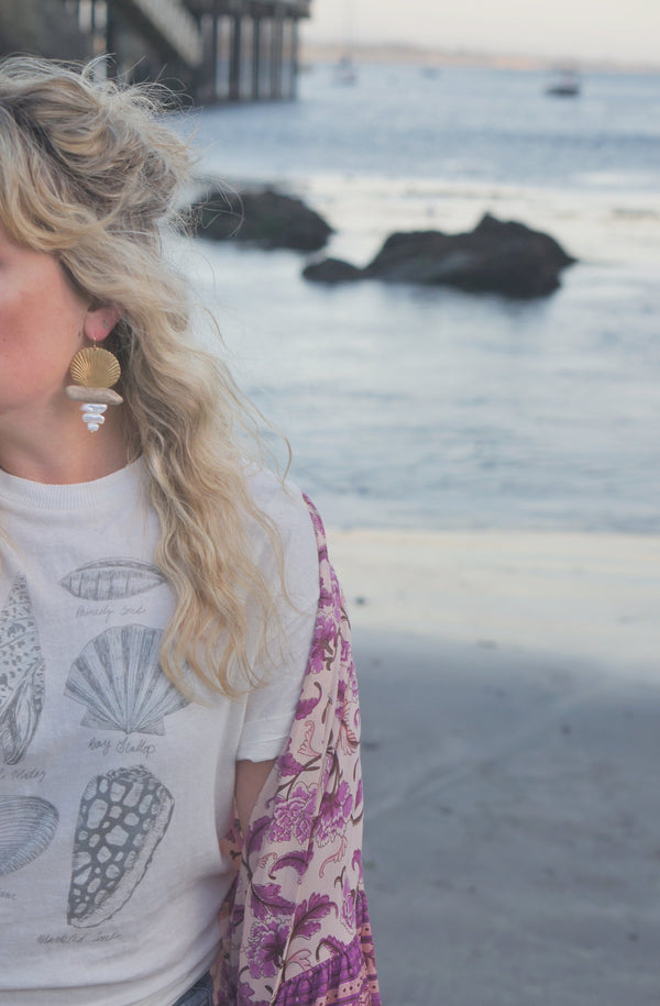 Gold shell, driftwood, and freshwater pearl earrings worn by woman with long blond hair wearing t shirt and kimono