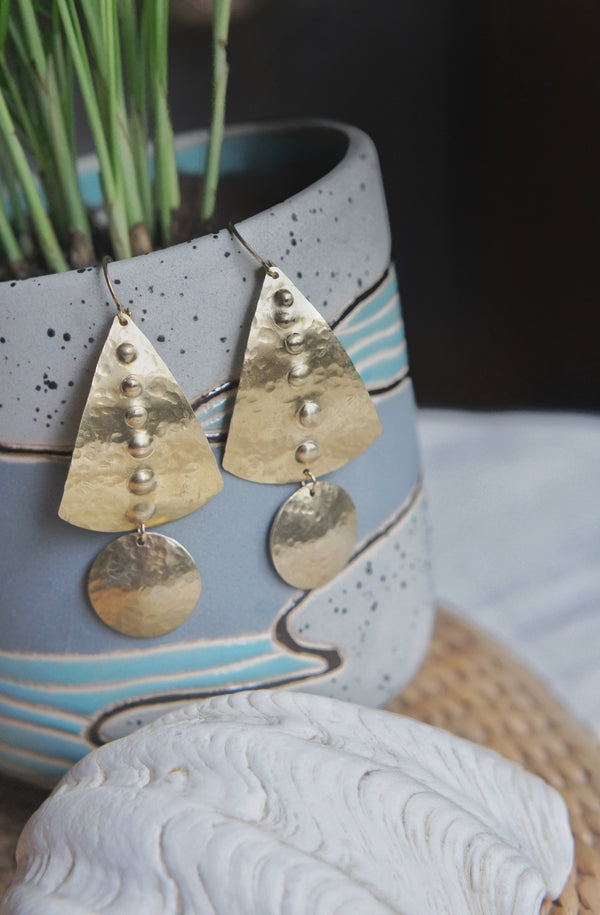 brass hammered earrings hanging on a potted plant